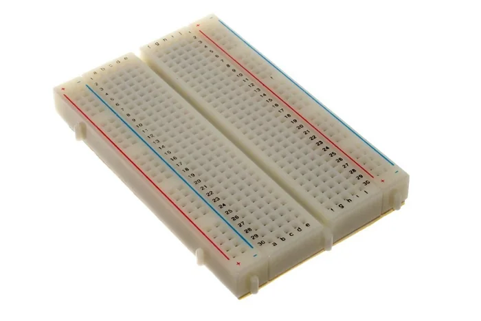 A solderless breadboard with rows of holes and red and blue power rails