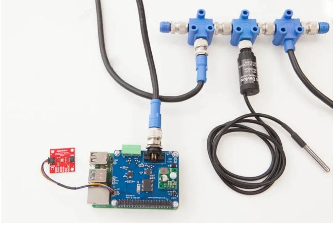 A PiCAN-M hat on a Raspberry Pi with an NMEA 2000 drop cable and blue T-connectors, a DS18B20 temperature probe and a small sensor board alongside